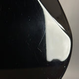 Close-up of a glossy black curved surface with visible scratches and a bright white reflection, against a light gray background.