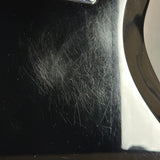 Close-up of a glossy black surface with visible scratches and wear, next to a bright white reflective area.
