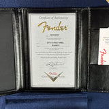 A Fender Certificate of Authenticity document displayed inside an open black leather portfolio folder lined with blue velvet. A small Fender card is visible on the right side.