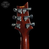 Close-up of the headstock of an electric guitar with a glossy dark reddish-brown wood finish, six silver tuning pegs, and yellow 'TONE SHOP' branding on the back, set against a solid black background.