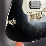 Close-up of a black electric guitar with visible wear on the body against a dark background
