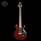 A double-cutaway electric guitar with a glossy reddish-brown flamed maple body, black pickguard, and maple neck, shown against a solid black background. A Tone Shop watermark is visible in the top-left corner.