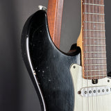 Close-up of a black electric guitar with a white pickguard on a gray background