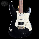 Black electric guitar with a worn finish on a black background, featuring the Tone Shop logo.