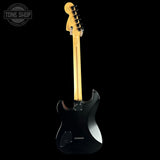 Black electric guitar with a wooden neck on a black background, featuring 'Tone Shop' branding.
