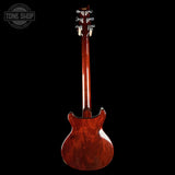 A back view of a double-cutaway electric guitar with a glossy reddish-brown wood finish, shown against a solid black background. A Tone Shop watermark is visible in the top-left corner.