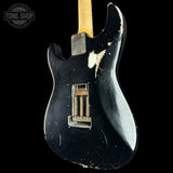 Black electric guitar with visible wear on a black background, featuring 'Tone Shop' logo.