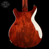 Close-up of the back of an electric guitar body with a rich reddish-brown wood finish and a white pickguard, shown against a black background.