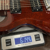 A close-up of a reddish-brown electric guitar body resting on a digital scale displaying 61.44 lbs.