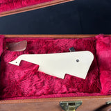 White guitar pickguard inside a case with red interior