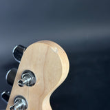Close-up detail of a light natural wood guitar headstock with silver tuning pegs against a dark blurred background.