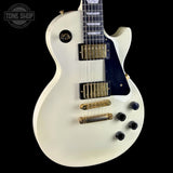 A white electric guitar with gold hardware and a black pickguard, shown against a solid black background. A Tone Shop watermark is visible in the top left corner.