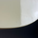 A close-up detail shot of a glossy off-white ceramic surface, showing a curved edge and a vertical seam with minor dust specks, set against a dark background.