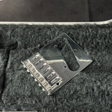 A shiny chrome metal guitar bridge assembly with six saddles, resting on a textured black felt surface.