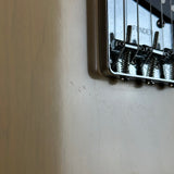 Close-up of a Fender bridge component mounted on a guitar body, shown against a beige wall background.