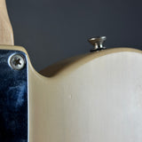 Close-up detail of an electric guitar body showing the cream-colored back, a dark blue pickguard, a silver screw, and a small metal knob against a dark gray background.
