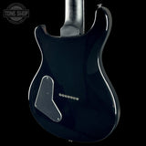 Close-up of the back of a glossy black electric guitar body against a black background, with a Tone Shop watermark in the upper left corner.
