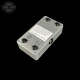 A silver metal guitar effects pedal or electronic module with four black knobs, a white specification label, and a 1/4-inch jack input, shown on a solid black background. A Tone Shop watermark is visible in the top-left corner.