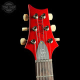Close-up of a red guitar headstock with tuning pegs on a black background, featuring the PRS logo.