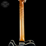 Close-up of a guitar's wooden neck with a black background, featuring the Tone Shop logo.