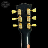 Close-up of a guitar headstock with tuning pegs on a black background, featuring the 'Tone Shop' logo.