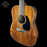 Acoustic guitar with a dark wood finish on a black background, featuring the Tone Shop logo.
