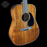 Acoustic guitar with a black pickguard on a black background, featuring the Tone Shop logo.