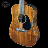 Acoustic guitar with a dark wood finish on a black background, featuring the Tone Shop logo.