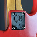 Close-up of a red electric guitar with a portrait engraving on the body.