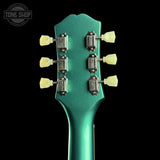 Close-up of a green guitar headstock with tuning pegs on a black background, featuring 'Tone Shop' branding.