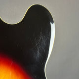 Close-up of a guitar's neck with a black pickguard and red fretboard against a gray background