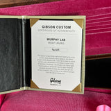 A Gibson Custom Certificate of Authenticity card for 'Murphy Lab Heavy Aging' is displayed inside an open gold-toned presentation case lined with bright pink velvet.