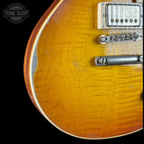 Close-up of the lower bout corner of a sunburst electric guitar body, showing the flamed maple wood grain, edge trim, bridge, and part of the pickup against a black background.