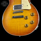 Close-up of a sunburst electric guitar body showing the maple top, black bridge, gold-toned pickups, and control knobs against a black background.