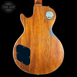 The back of a vintage Gibson electric guitar with a warm brown wood finish, showing the backplate, pickguard, and original headstock sticker on a black background.