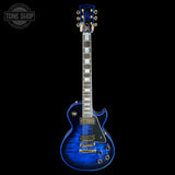 A blue flamed maple electric guitar with gold hardware, shown from the front against a solid black background. A 'TONE SHOP' watermark is visible in the top-left corner.