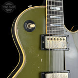 Close-up of a vintage-style electric guitar body in olive green with black and gold binding, showing part of the fretboard, pickups, and a Tone Shop logo watermark in the top left corner.