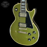 A distressed olive green electric guitar with a black pickguard and gold trim, shown against a solid black background. A Tone Shop watermark is visible in the top left corner.