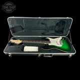 An electric guitar with a green-to-brown sunburst finish and white pickguard, displayed inside an open black hard case on a black background. A Tone Shop watermark is visible in the top left corner.