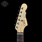 Close-up of the headstock of a Fender Legacy Stratocaster electric guitar against a solid black background. The headstock features a natural light wood finish with silver tuning pegs and a dark brown wood fretboard visible at the bottom.