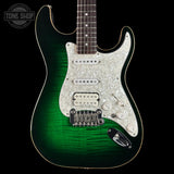 A G&L Stratocaster electric guitar with a green-to-clear flame finish, a white mother-of-pearl pickguard, and chrome hardware, shown against a solid black background.