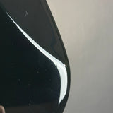 Close-up of a glossy black curved surface with a white highlight and visible dust particles, against a plain light gray background.