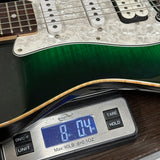 A close-up of a green electric guitar body resting on a digital scale to measure its weight, with the scale displaying 8.04 lbs.