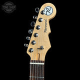 Close-up of the headstock of a Reverend six-string electric guitar in natural wood, featuring six chrome tuning pegs and a black logo decal, set against a solid black background.