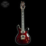 Electric guitar with a dark finish on a black background, featuring the Tone Shop logo.