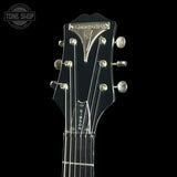 Close-up of a black electric guitar headstock with six silver tuning pegs and strings, featuring the 'TONE SHOP' logo in the top-left corner against a solid black background.