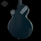 The back of a glossy dark blue electric guitar, featuring a double-cutaway body shape, a clear plastic pickguard, and a circular soundhole cover, shown against a solid black background.