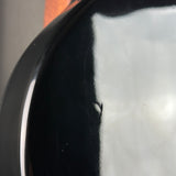 Close-up of a glossy black curved surface with a reflective white highlight and a small visible scratch or defect on the dark area.