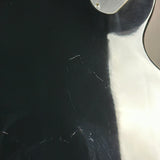 Close-up of a glossy black guitar body with visible scratches and a light reflection on the right side.