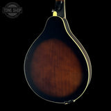 Close-up of the back of a mandolin with a dark brown sunburst finish and cream-colored binding, shown against a solid black background with a Tone Shop watermark in the top-left corner.
